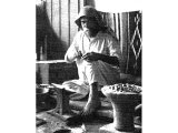 In this cupboard-like workshop the silversmith fashions all kinds of delicate pieces of his ware on his anvil. On the right is the earthenware brazier in which the metal is treated. An early photograph.